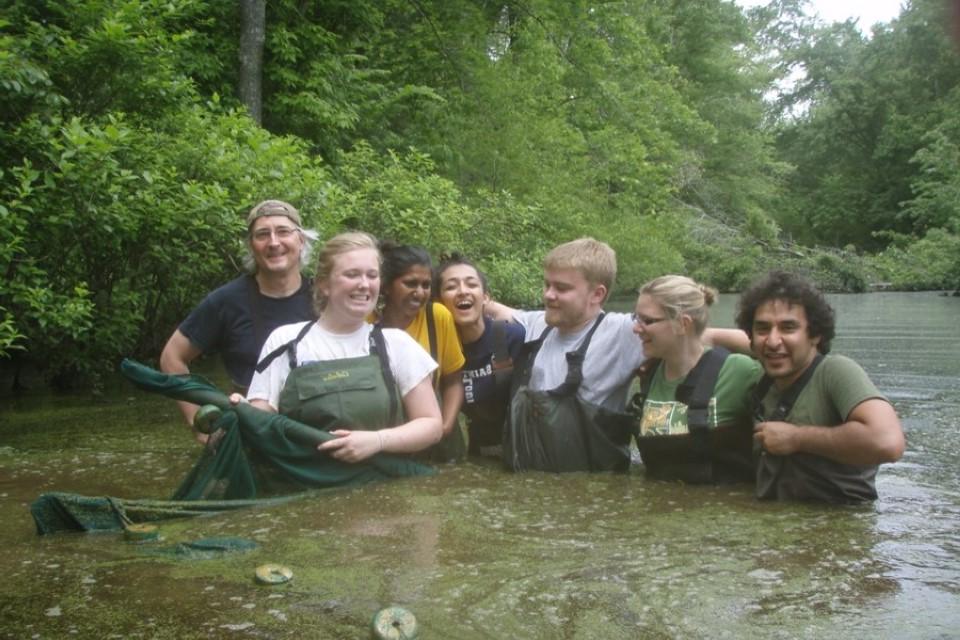 Seven students stand in water, wearing hip waders