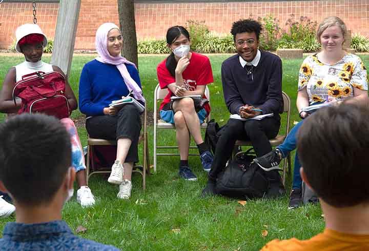 一群学生坐在草坪上围成一圈的折叠椅上讨论