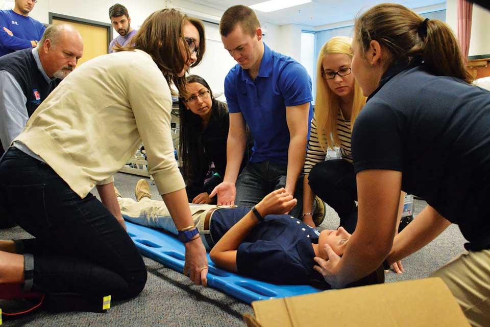 A student lies on a back board surrounded by other students and instructors during a demonstration.