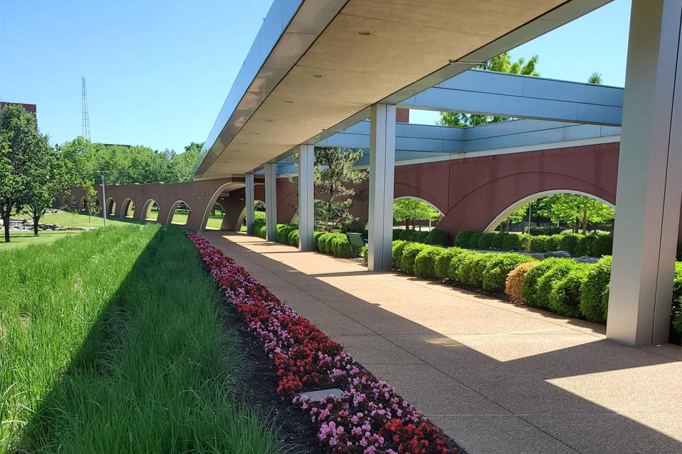 A covered walkway lined by flowers and greenery.