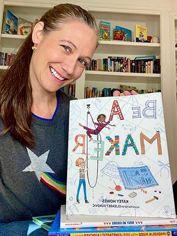 作者凯蒂·豪斯, 一位留着深色长发的中年妇女, 穿着一件有星星的毛衣，手里拿着她孩子的图画书, Be a Maker.