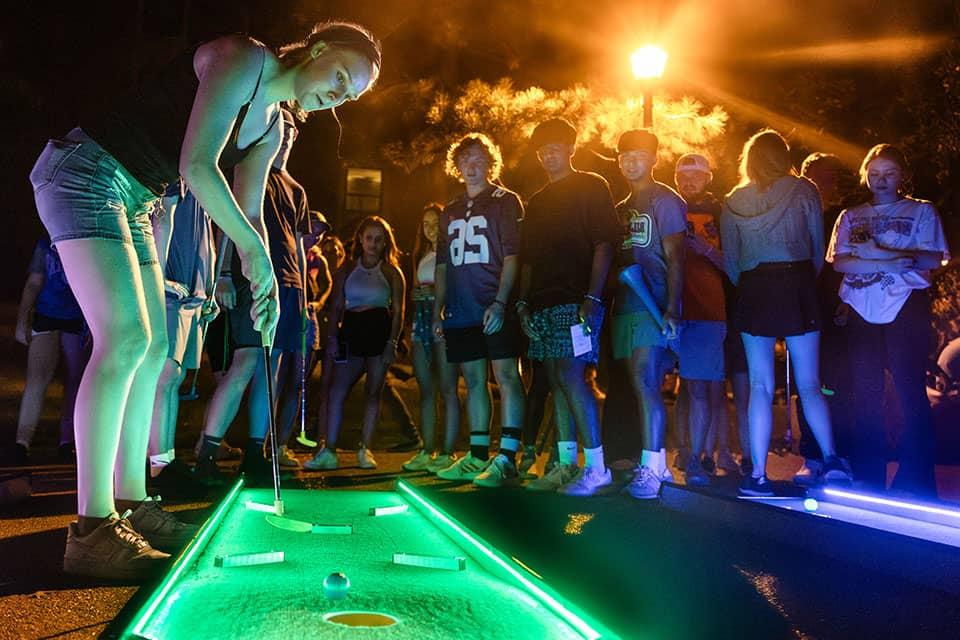 在一年一度的街头派对上，一名学生在灯火通明的高尔夫球场上打迷你高尔夫球.